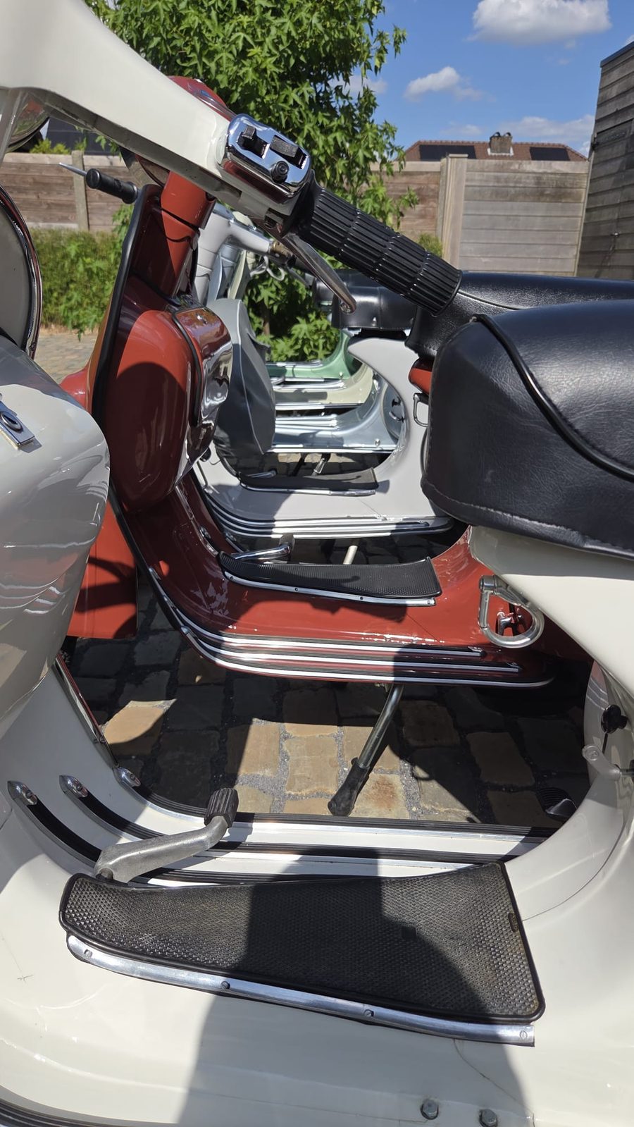 Detail van de treeplanken en het stuur van een rode en een cr&egrave;mekleurige Vespa