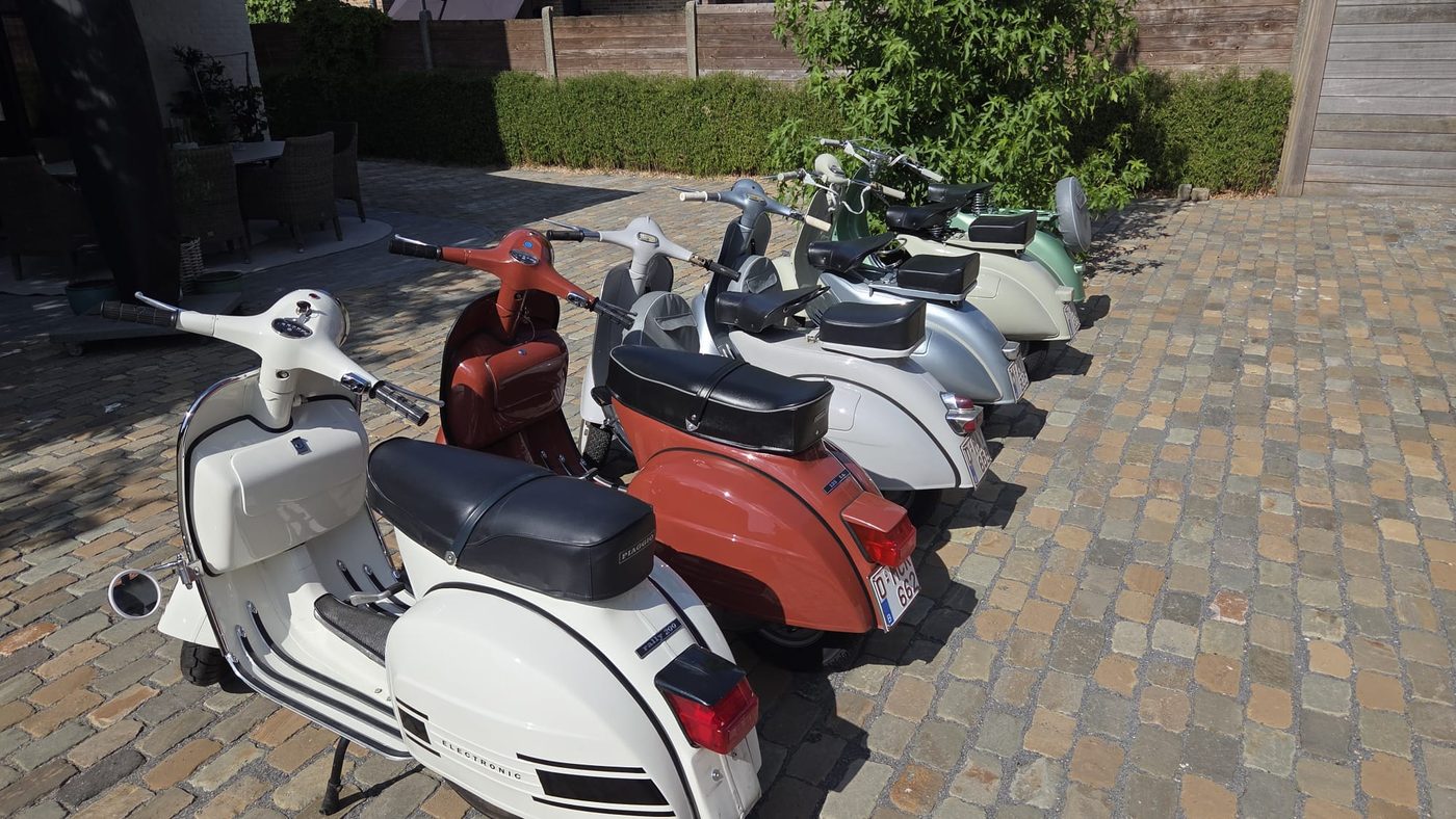 Dezelfde zes Vespa's schuin van achteren, met de zadels in de zon